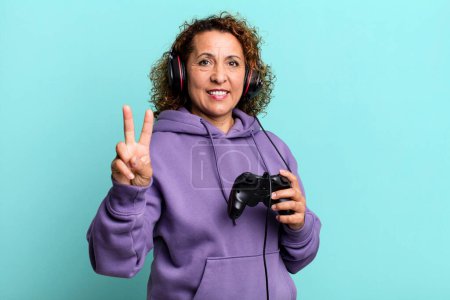 Photo for Pretty middle age woman smiling and looking friendly, showing number two playing virtual game. gamer concept - Royalty Free Image
