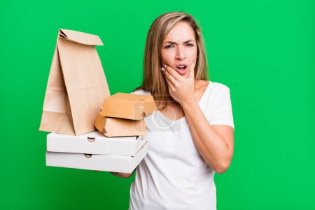 Téléchargez les photos : Pretty blonde woman with mouth and eyes wide open and hand on chin. delivery take away food packages concept - en image libre de droit