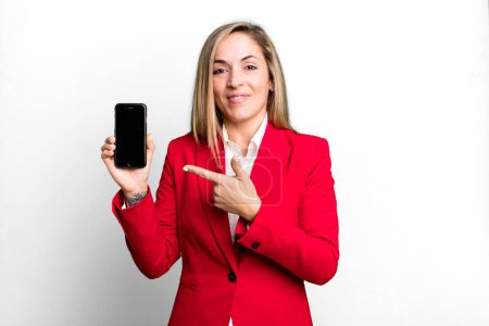 Photo for Pretty blonde woman smiling cheerfully, feeling happy and pointing to the side. businesswoman and a phone concept - Royalty Free Image