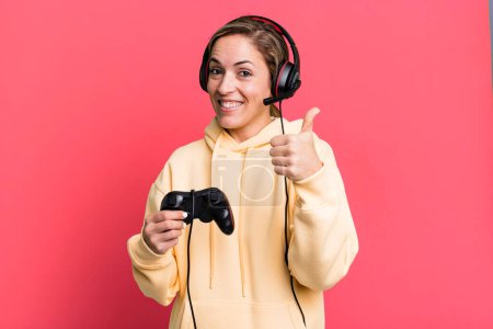 Photo for Pretty blonde woman feeling proud,smiling positively with thumbs up. gamer with headset and a controller - Royalty Free Image
