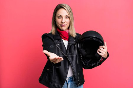 Foto de Pretty blonde woman smiling happily with friendly and  offering and showing a concept. motorbike rider and helmet concept - Imagen libre de derechos