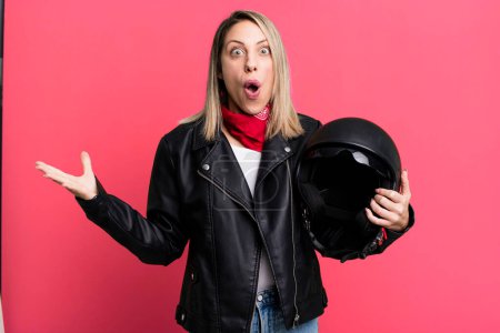 Foto de Pretty blonde woman feeling extremely shocked and surprised. motorbike rider and helmet concept - Imagen libre de derechos