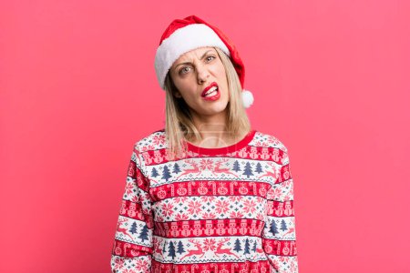 Foto de Bonita mujer rubia sintiéndose perpleja y confundida. concepto de Navidad y sombrero de santa - Imagen libre de derechos