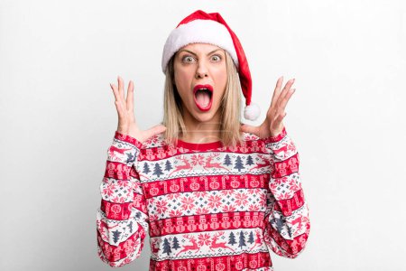 Téléchargez les photos : Pretty blonde woman screaming with hands up in the air. christmas and santa hat concept - en image libre de droit