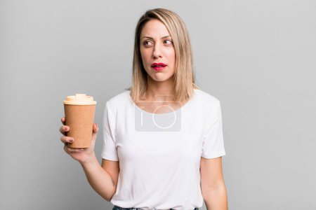 Téléchargez les photos : Pretty blonde woman feeling sad, upset or angry and looking to the side with a hot coffee - en image libre de droit