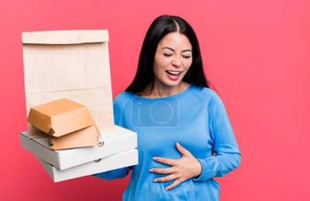 Photo for Hispanic pretty woman laughing out loud at some hilarious joke. with take away fast food packages - Royalty Free Image