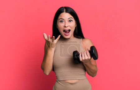 Photo for Hispanic pretty woman looking desperate, frustrated and stressed. fitness concept and dumbbell - Royalty Free Image