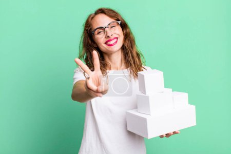 Photo for Hispanic pretty woman smiling and looking happy, gesturing victory or peace. with white boxes packages - Royalty Free Image
