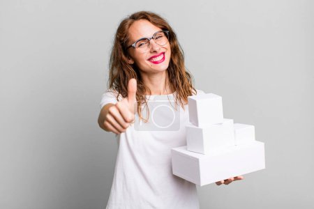 Photo for Hispanic pretty woman feeling proud,smiling positively with thumbs up. with white boxes packages - Royalty Free Image