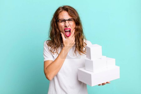 Photo for Hispanic pretty woman with mouth and eyes wide open and hand on chin. with white boxes packages - Royalty Free Image
