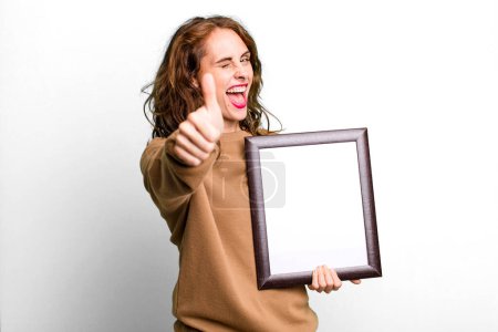 Photo for Hispanic pretty woman feeling proud,smiling positively with thumbs up with an empty blank frame - Royalty Free Image