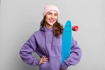 Téléchargez les photos : Hispanique jolie femme souriant joyeusement avec une main sur la hanche et confiant. concept de skate board - en image libre de droit