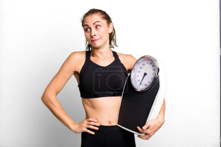 Photo for Hispanic pretty woman shrugging, feeling confused and uncertain. fitness, diet and weight scale concept - Royalty Free Image