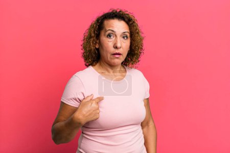 Photo for Middle age hispanic woman feeling confused, puzzled and insecure, pointing to self wondering and asking who, me? - Royalty Free Image