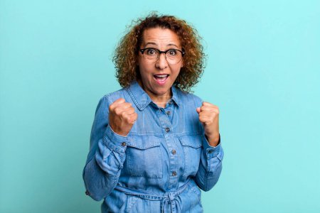 Photo for Middle age hispanic woman feeling shocked, excited and happy, laughing and celebrating success, saying wow! - Royalty Free Image