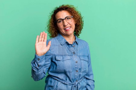 Photo for Middle age hispanic woman smiling happily and cheerfully, waving hand, welcoming and greeting you, or saying goodbye - Royalty Free Image