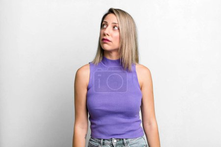 Photo for Blonde adult woman with a worried, confused, clueless expression, looking up to copy space, doubting - Royalty Free Image