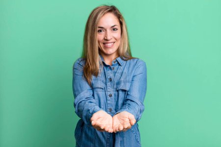 Photo for Blonde adult woman smiling happily with friendly, confident, positive look, offering and showing an object or concept - Royalty Free Image