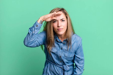 Photo for Blonde adult woman looking bewildered and astonished, with hand over forehead looking far away, watching or searching - Royalty Free Image