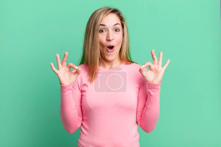 Photo for Blonde adult woman feeling shocked, amazed and surprised, showing approval making okay sign with both hands - Royalty Free Image