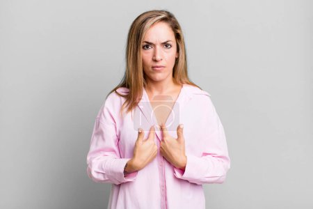 Photo for Blonde adult woman pointing to self with a confused and quizzical look, shocked and surprised to be chosen - Royalty Free Image