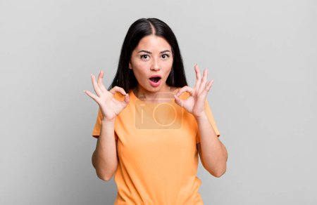 Foto de Pretty latin woman feeling shocked, amazed and surprised, showing approval making okay sign with both hands - Imagen libre de derechos