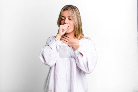 Téléchargez les photos : Blonde jolie femme se sentant malade avec un mal de gorge et des symptômes de grippe, toux avec la bouche couverte - en image libre de droit