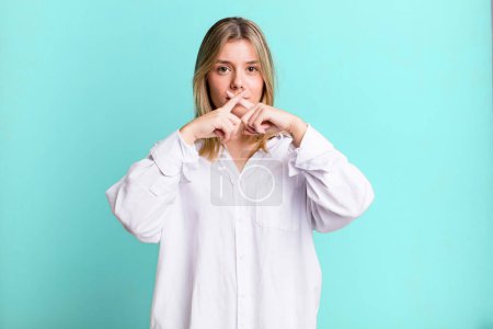 Photo for Blonde pretty woman looking serious and displeased with both fingers crossed up front in rejection, asking for silence - Royalty Free Image