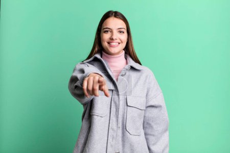 Photo for Pretty young adult woman pointing at camera with a satisfied, confident, friendly smile, choosing you - Royalty Free Image