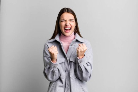 Téléchargez les photos : Pretty young adult woman shouting aggressively with annoyed, frustrated, angry look and tight fists, feeling furious - en image libre de droit