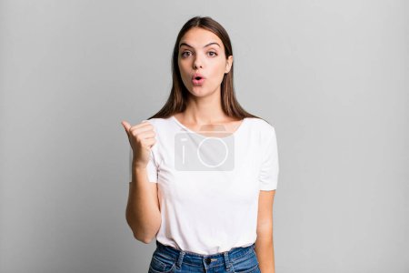 Téléchargez les photos : Pretty young adult woman looking astonished in disbelief, pointing at object on the side and saying wow, unbelievable - en image libre de droit