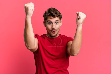 Foto de Young adult caucasian man celebrating an unbelievable success like a winner, looking excited and happy saying take that! - Imagen libre de derechos