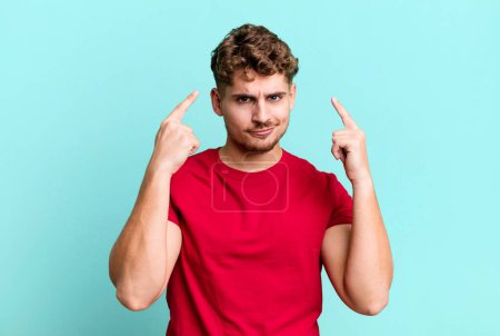 Téléchargez les photos : Young adult caucasian man with a bad attitude looking proud and aggressive, pointing upwards or making fun sign with hands - en image libre de droit