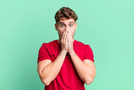 Téléchargez les photos : Young adult caucasian man feeling worried, upset and scared, covering mouth with hands, looking anxious and having messed up - en image libre de droit