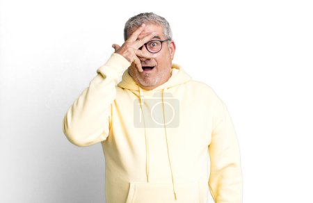 Photo for Middle age senior man looking shocked, scared or terrified, covering face with hand and peeking between fingers - Royalty Free Image