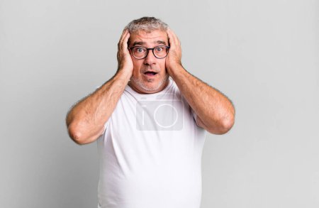 Photo for Middle age senior man looking unpleasantly shocked, scared or worried, mouth wide open and covering both ears with hands - Royalty Free Image