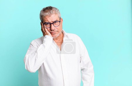 Téléchargez les photos : Homme âgé d'âge moyen se sentant ennuyé, frustré et somnolent après une tâche fatigante, ennuyeux et fastidieux, tenant le visage avec la main - en image libre de droit