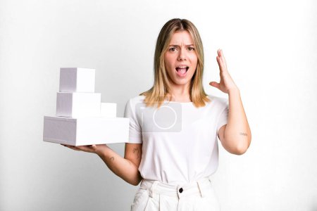 Photo for Young pretty woman screaming with hands up in the air. blank white boxes concept - Royalty Free Image