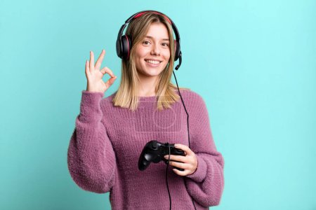 Téléchargez les photos : Young pretty woman feeling happy, showing approval with okay gesture. gamer with headset and controller - en image libre de droit