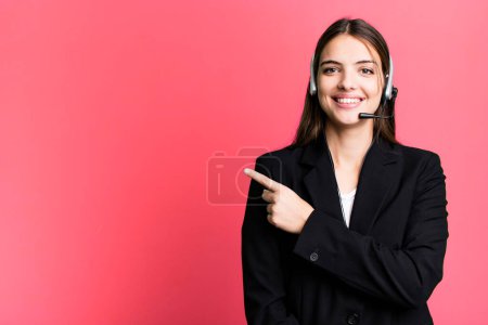 Foto de Joven bonita mujer sonriendo alegremente, sintiéndose feliz y señalando hacia un lado. concepto de agente de telemarketing - Imagen libre de derechos