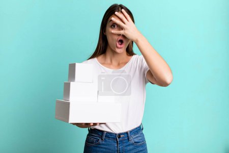 Photo for Young pretty woman looking shocked, scared or terrified, covering face with hand. blank white boxes - Royalty Free Image