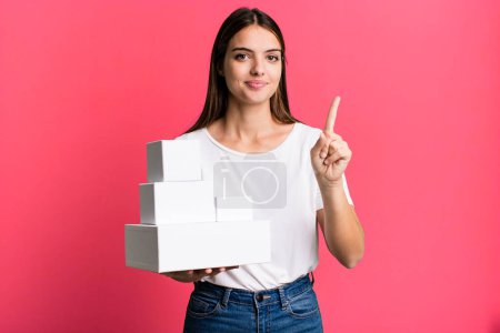 Photo for Young pretty woman smiling and looking friendly, showing number one. blank white boxes - Royalty Free Image