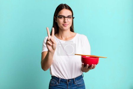 Photo for Young pretty woman smiling and looking friendly, showing number two. japanese ramen noodles concept - Royalty Free Image