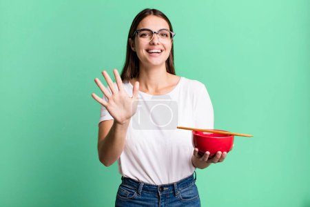 Photo for Young pretty woman smiling and looking friendly, showing number five. japanese ramen noodles concept - Royalty Free Image