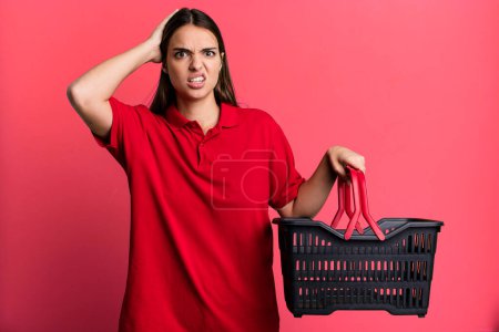 Téléchargez les photos : Young pretty woman feeling stressed, anxious or scared, with hands on head. empty shopping basket concept - en image libre de droit
