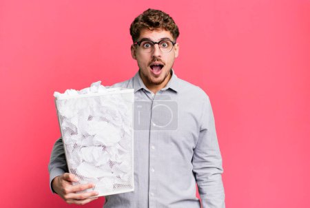 Photo for Young adult caucasian man looking very shocked or surprised with a paper balls trash concept - Royalty Free Image