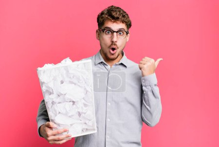 Photo for Young adult caucasian man looking astonished in disbelief with a paper balls trash concept - Royalty Free Image