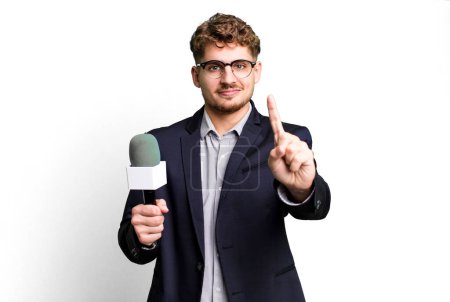 Foto de Young adult caucasian man smiling and looking friendly, showing number one. journalist or presenter with a microphone - Imagen libre de derechos