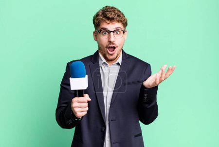 Foto de Young adult caucasian man feeling extremely shocked and surprised. journalist or presenter with a microphone - Imagen libre de derechos