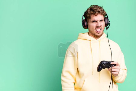 Foto de Young adult caucasian man feeling disgusted and irritated and tongue out with headset and a controller. gamer concept - Imagen libre de derechos